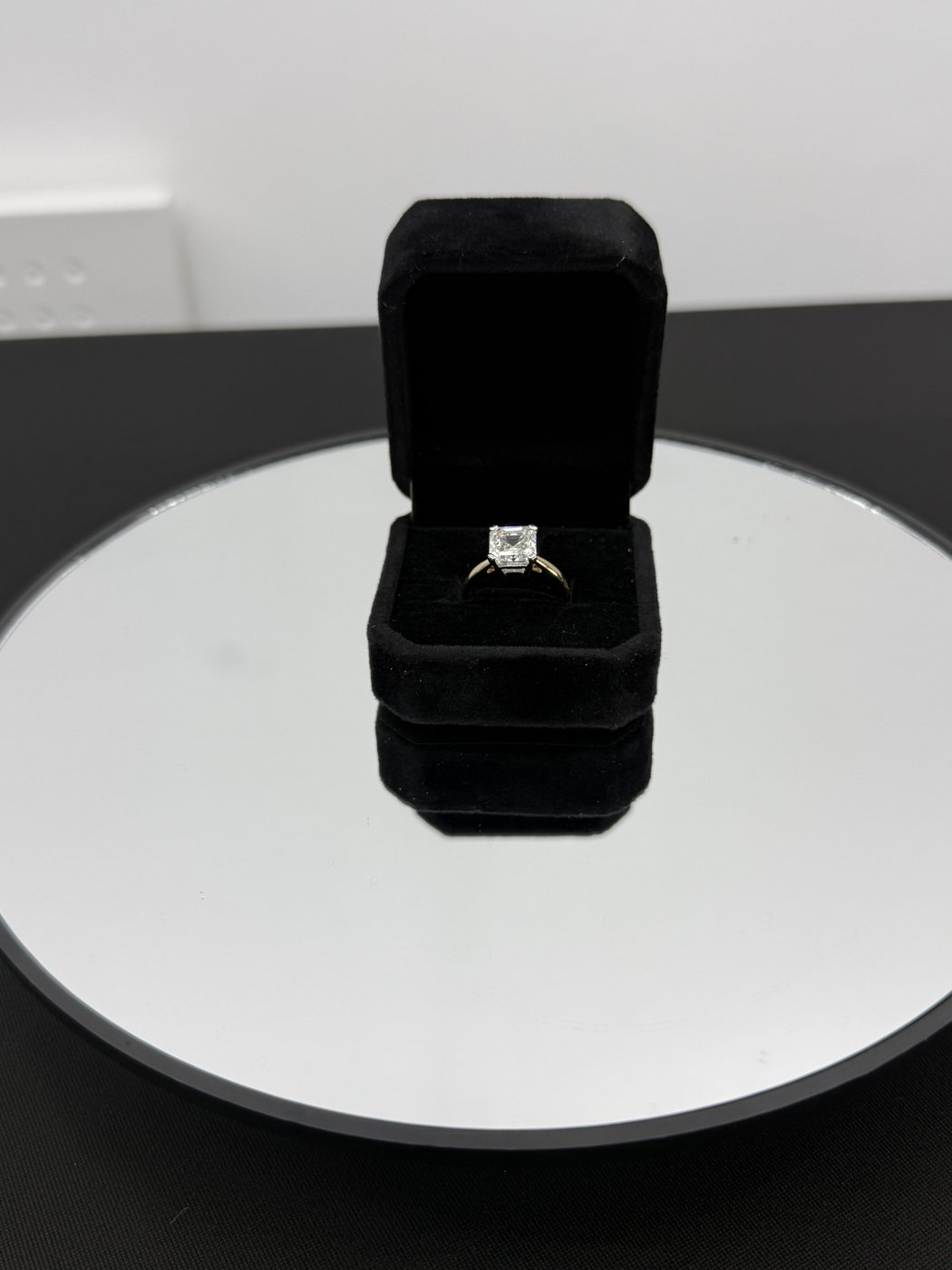 Solitaire ring presented in a black box on a mirrored stand