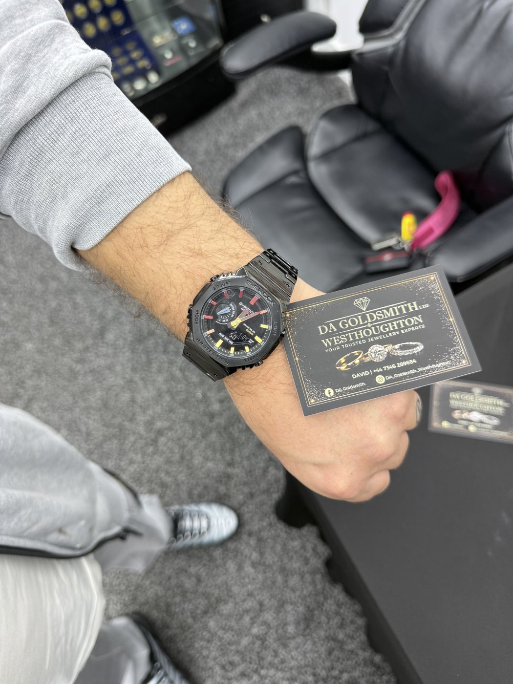 Dark watch worn on a wrist beside a DA Goldsmith card